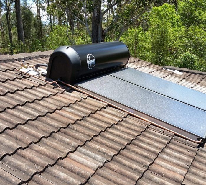 A Black Water Heater is Sitting on Top of a Tiled Roof — Solar Services in Bateau Bay, NSW