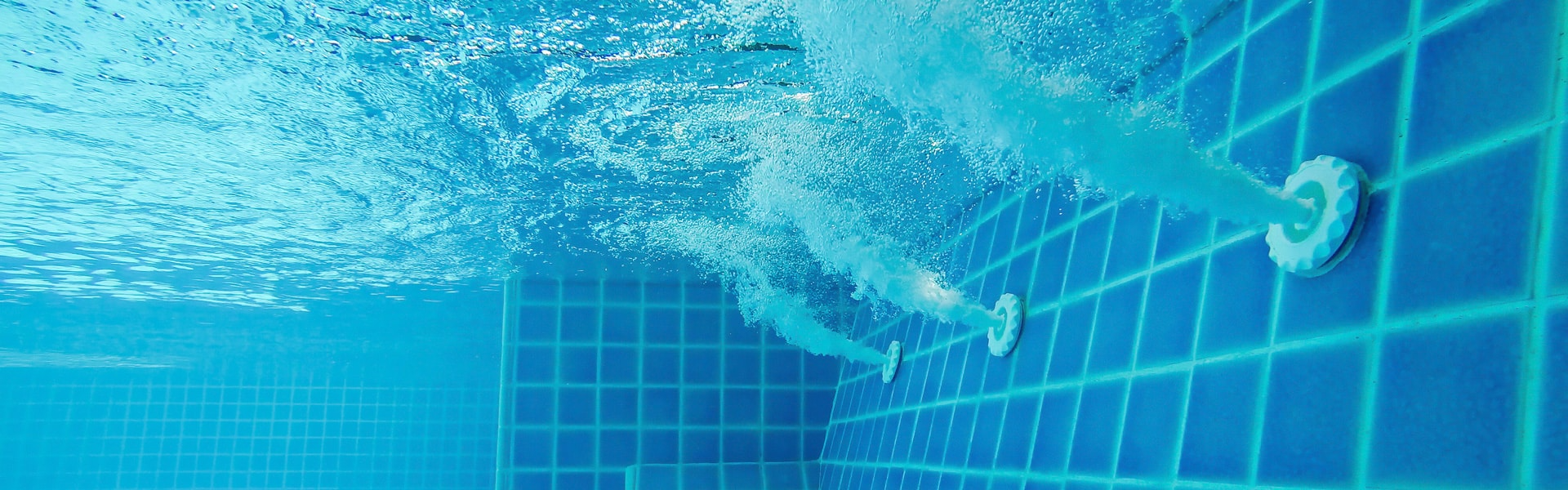 Underwater view of a blue tiled pool with jets creating bubbly water — Solar Services in Erina, NSW