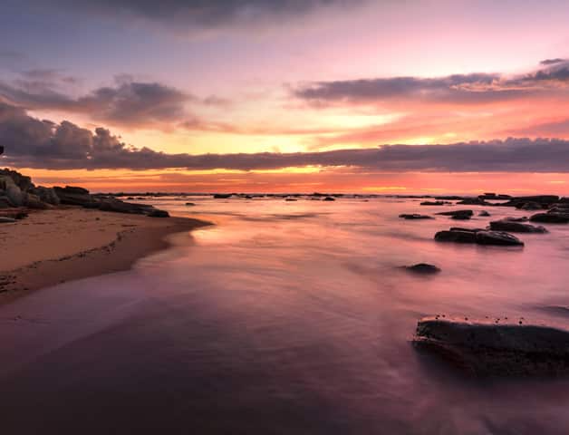 The Sun is Setting Over the Ocean With Rocks in the Foreground — Solar Services in Bateau Bay, NSW