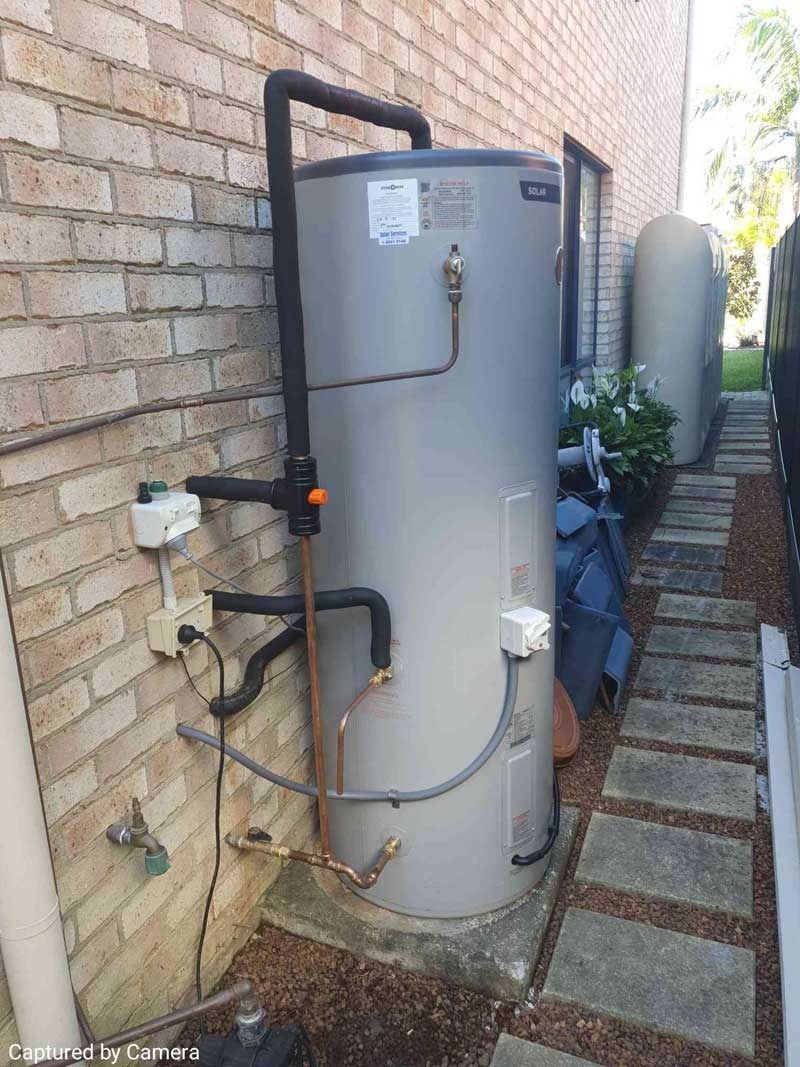 A Water Heater is Attached to the Side of a Brick Building — Solar Services in Erina, NSW