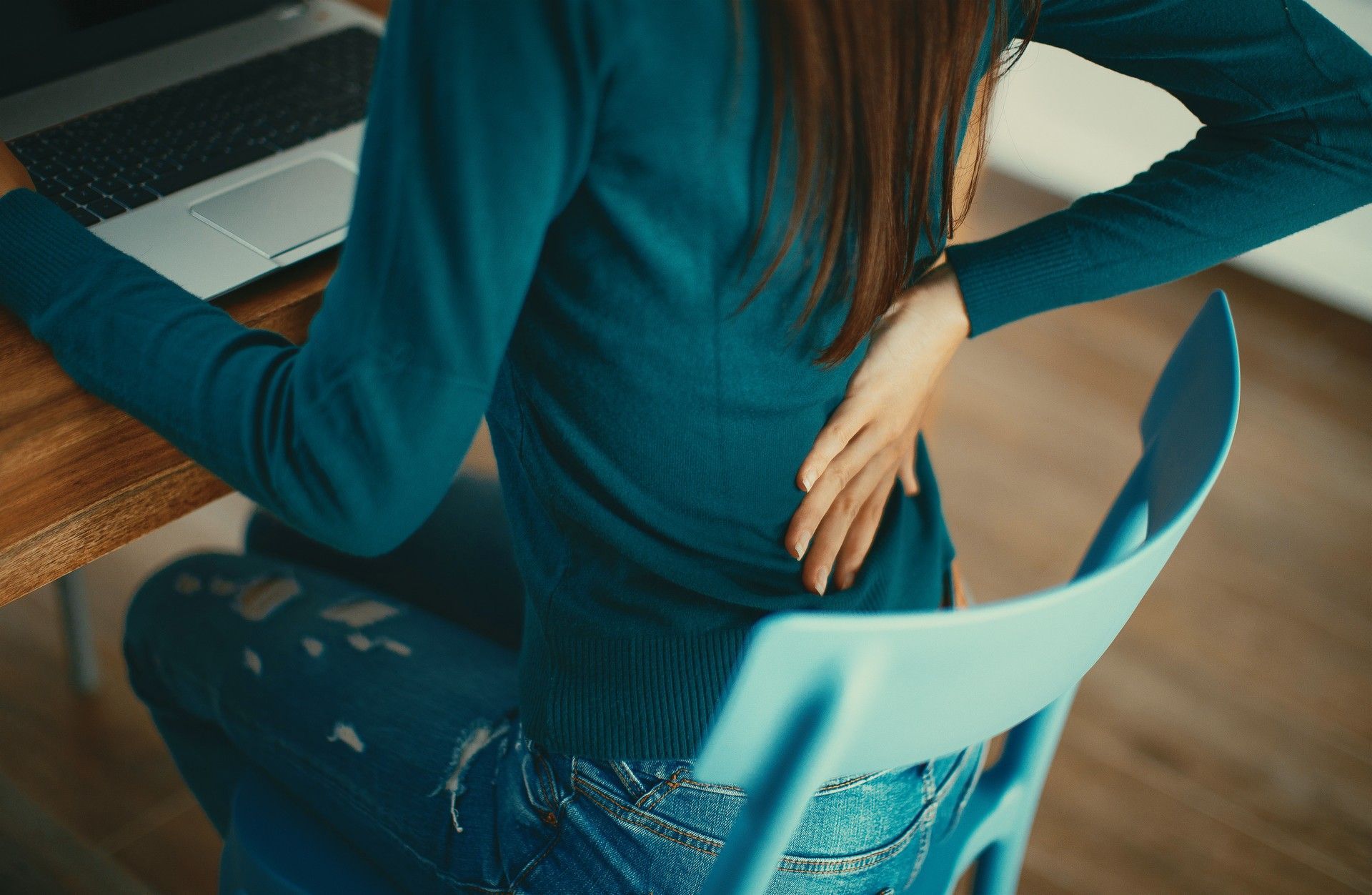 Una donna è seduta alla scrivania con un computer portatile e si tiene la schiena.