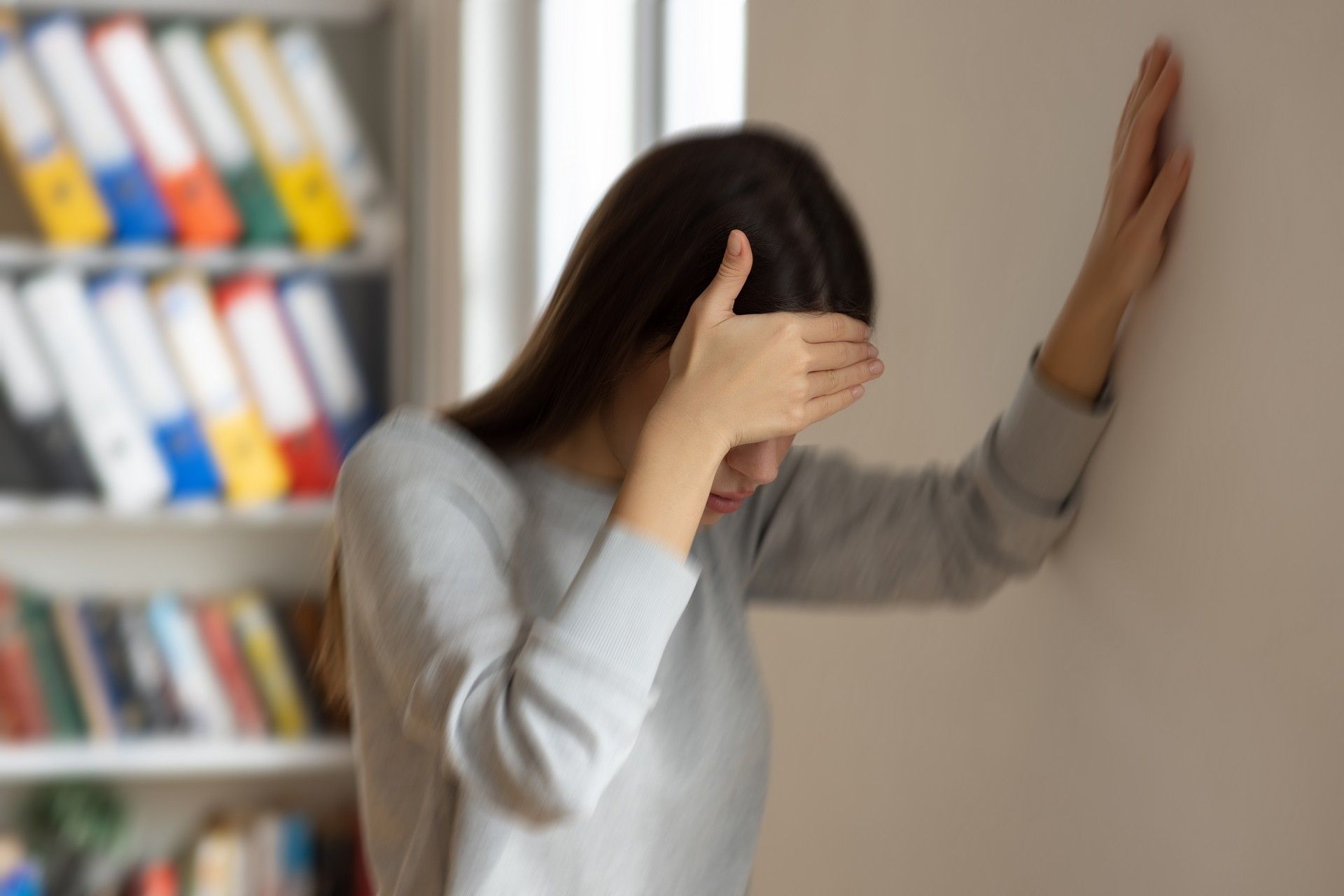 Una donna si copre il viso con la mano mentre è appoggiata a un muro.