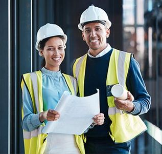 Two construction workers in hard hats and safety vests reviewing blueprints at a job site