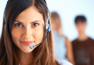 Smiling customer support agent wearing a headset, with two blurred people in the background