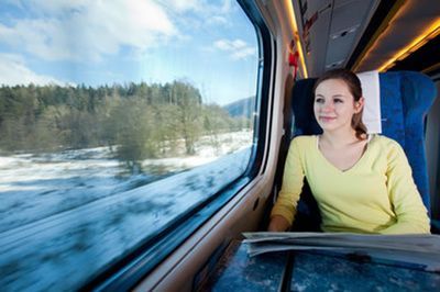 Woman sitting by a train window, looking out at snowy trees passing by.