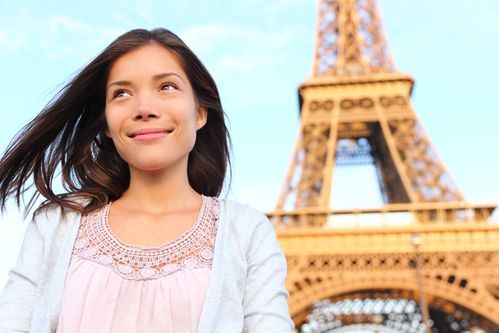 Woman smiling in front of the Eiffel Tower in Paris, with windblown hair and a light blouse.