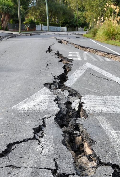 Cracked road with a large sinkhole splitting the asphalt on a street near greenery