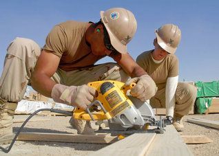 Two workers in hard hats using a circular saw on wood at a construction site