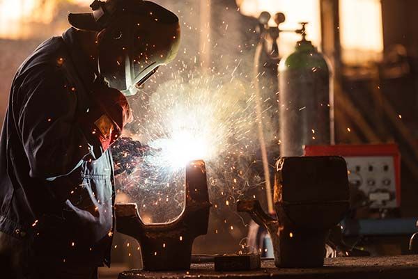Welder in protective gear sparks metal in a dim workshop