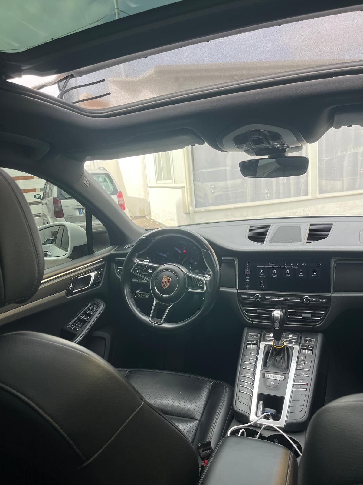Interni di un SUV Porsche: sedili in pelle nera, cruscotto, volante, tettuccio apribile e vista attraverso il parabrezza.