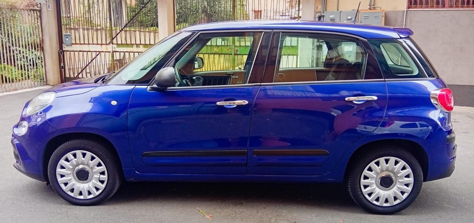 Fiat 500L blu parcheggiata all'esterno. La vista laterale mostra cerchi argentati, finiture nere e tetto alto.