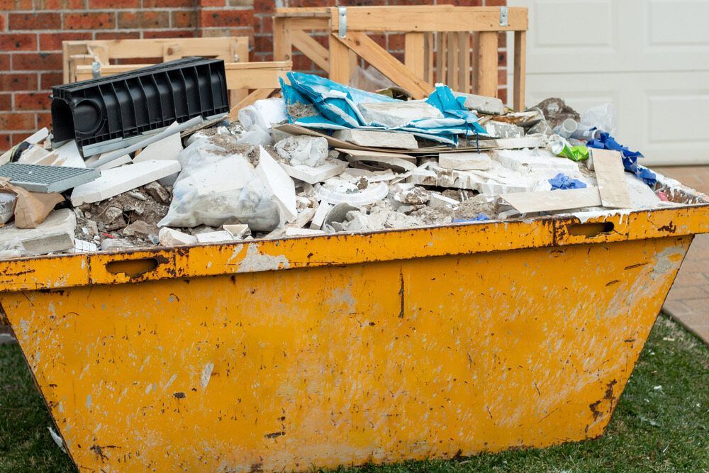 Yellow Dumpster Overflowing With Construction Debris in Front of a Brick House — Hasti Skips in Alstonville, NSW