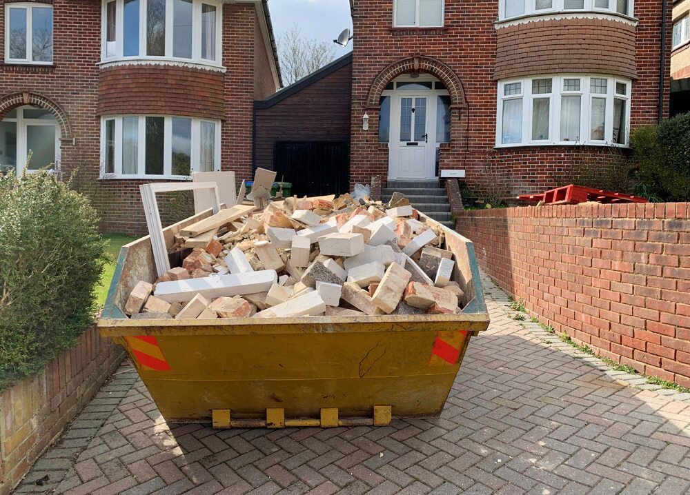 Dumpster Filled With Construction Debris Sits on a Brick Driveway in Front of a Red Brick House — Hasti Skips in Lismore, NSW