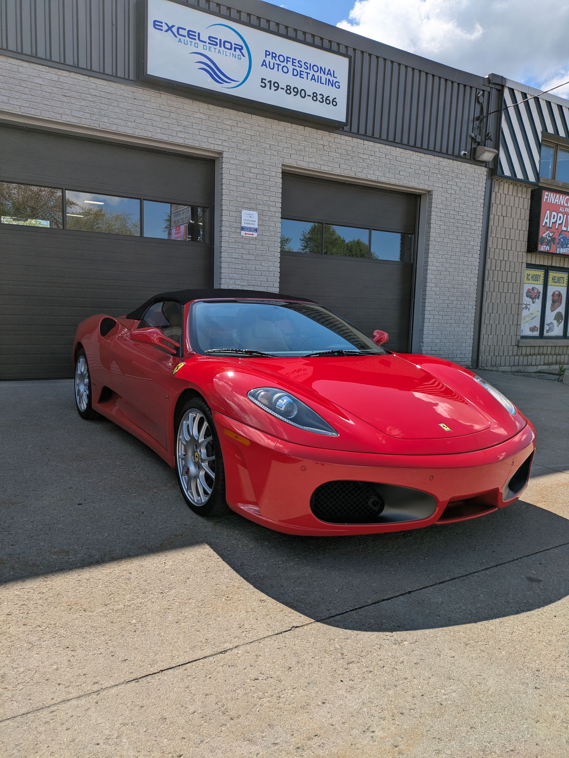 Red Ferrari convertible parked in front of a grey auto shop.