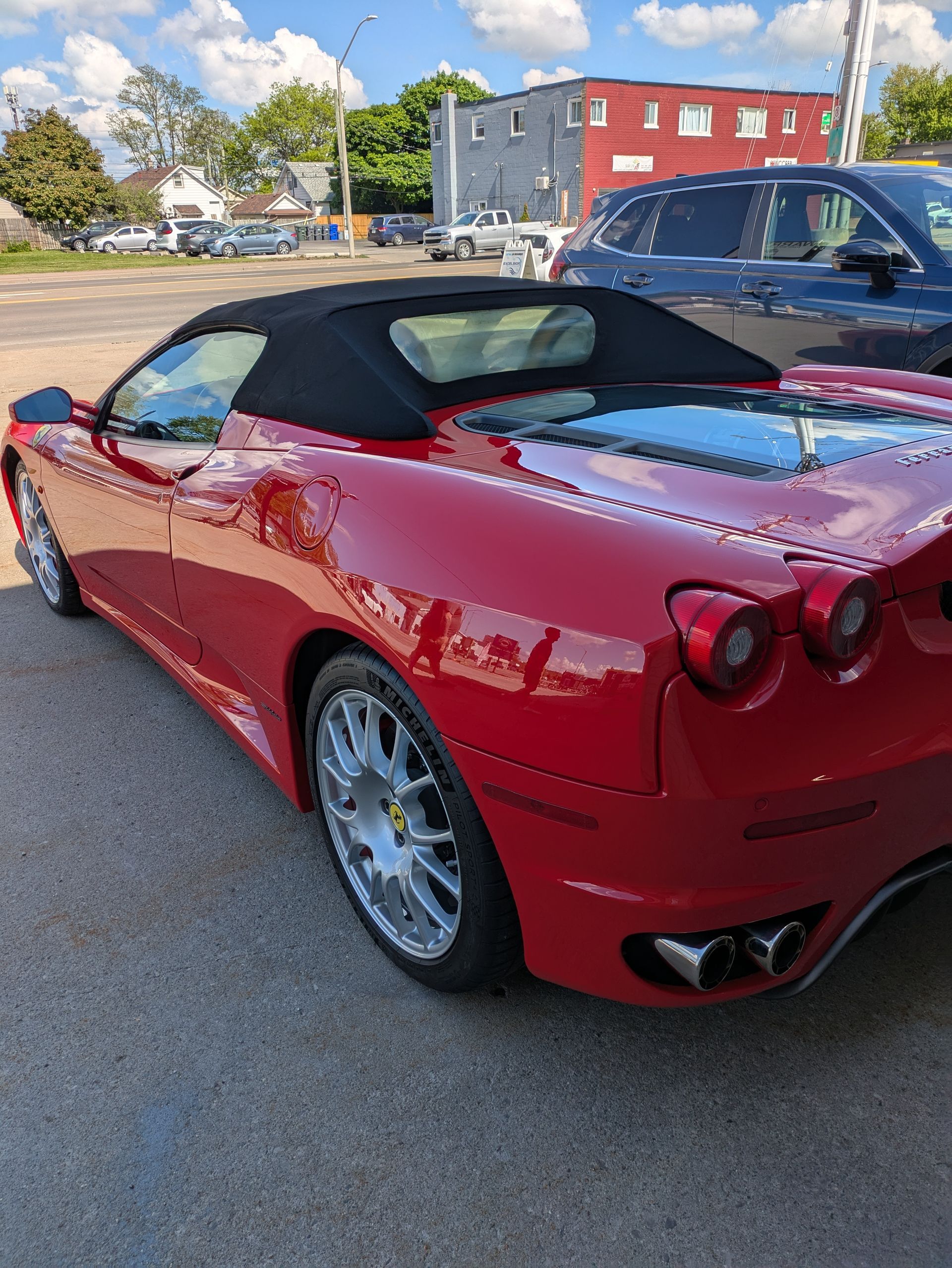 Red convertible Ferrari with a black top parked on a street, sunny day.