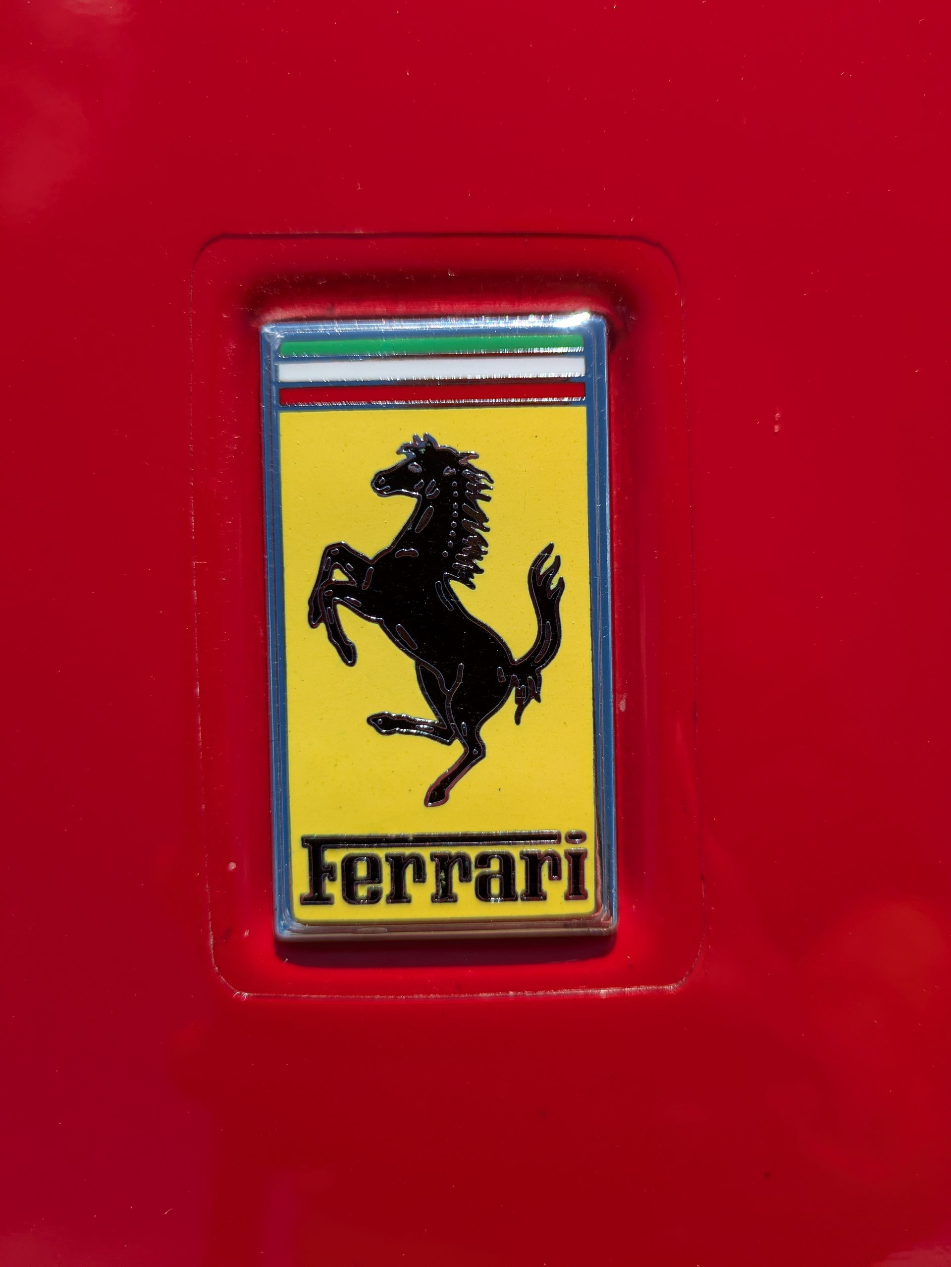 Ferrari emblem: black prancing horse on yellow, Italian flag colors, red background.