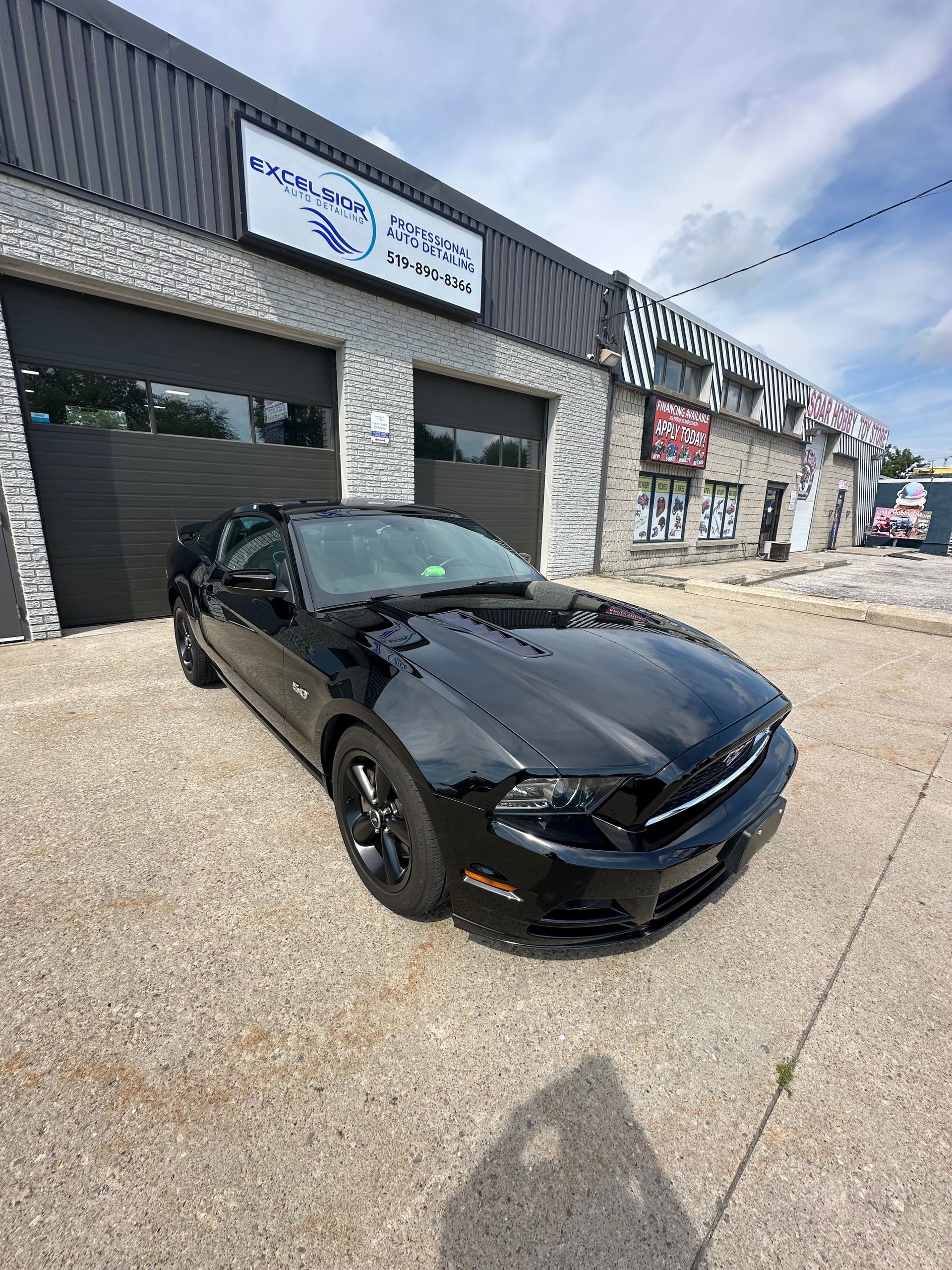 Black Ford Mustang in front of a brick building with a sign reading