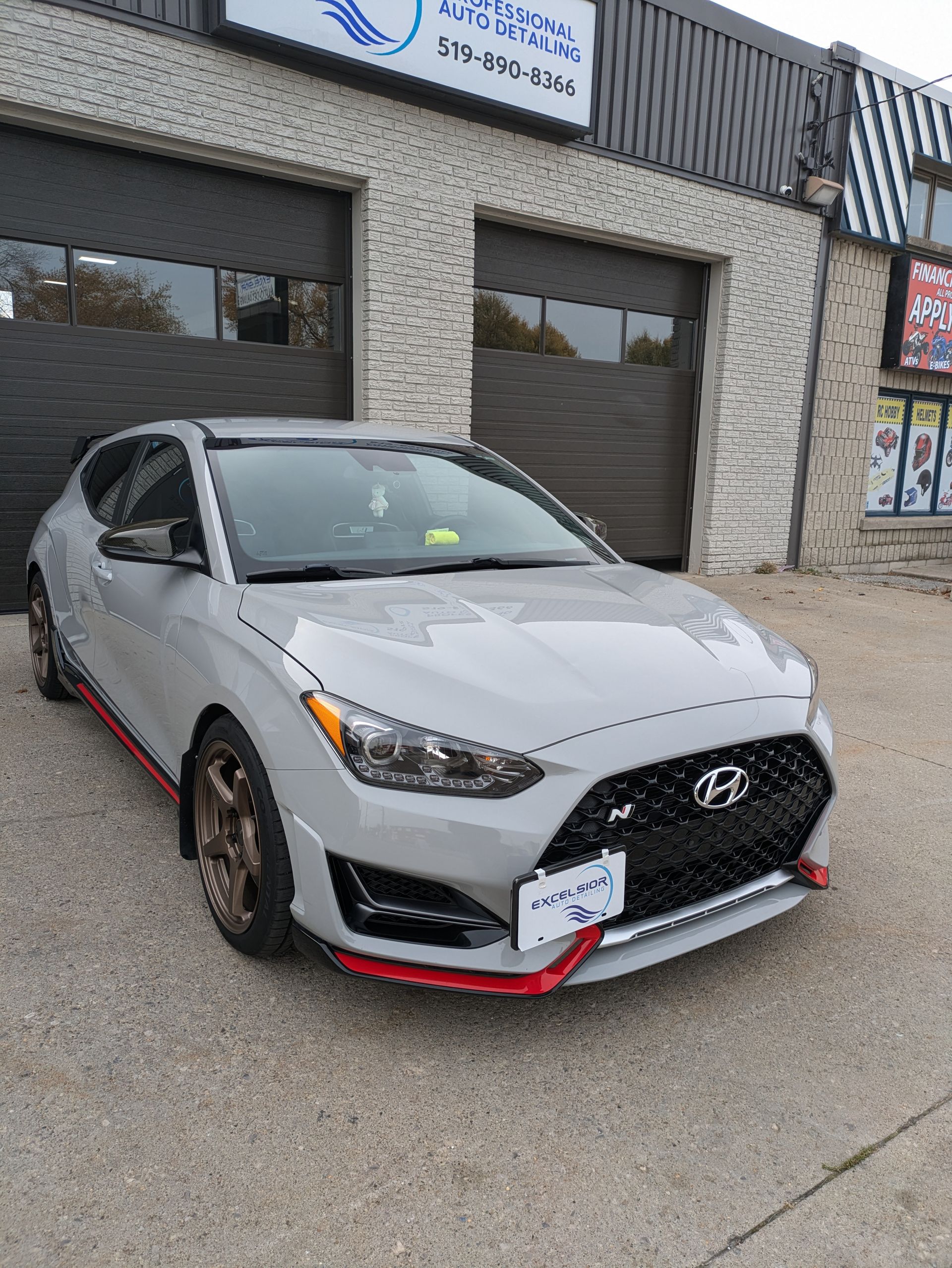 A silver hyundai veloster is parked in front of a garage.