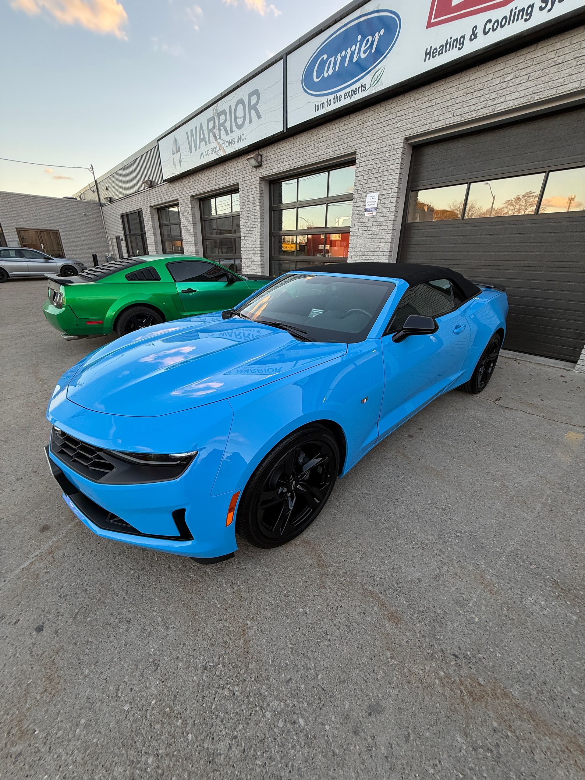 Bright blue sports car parked outside a storefront, with a green car beside it.