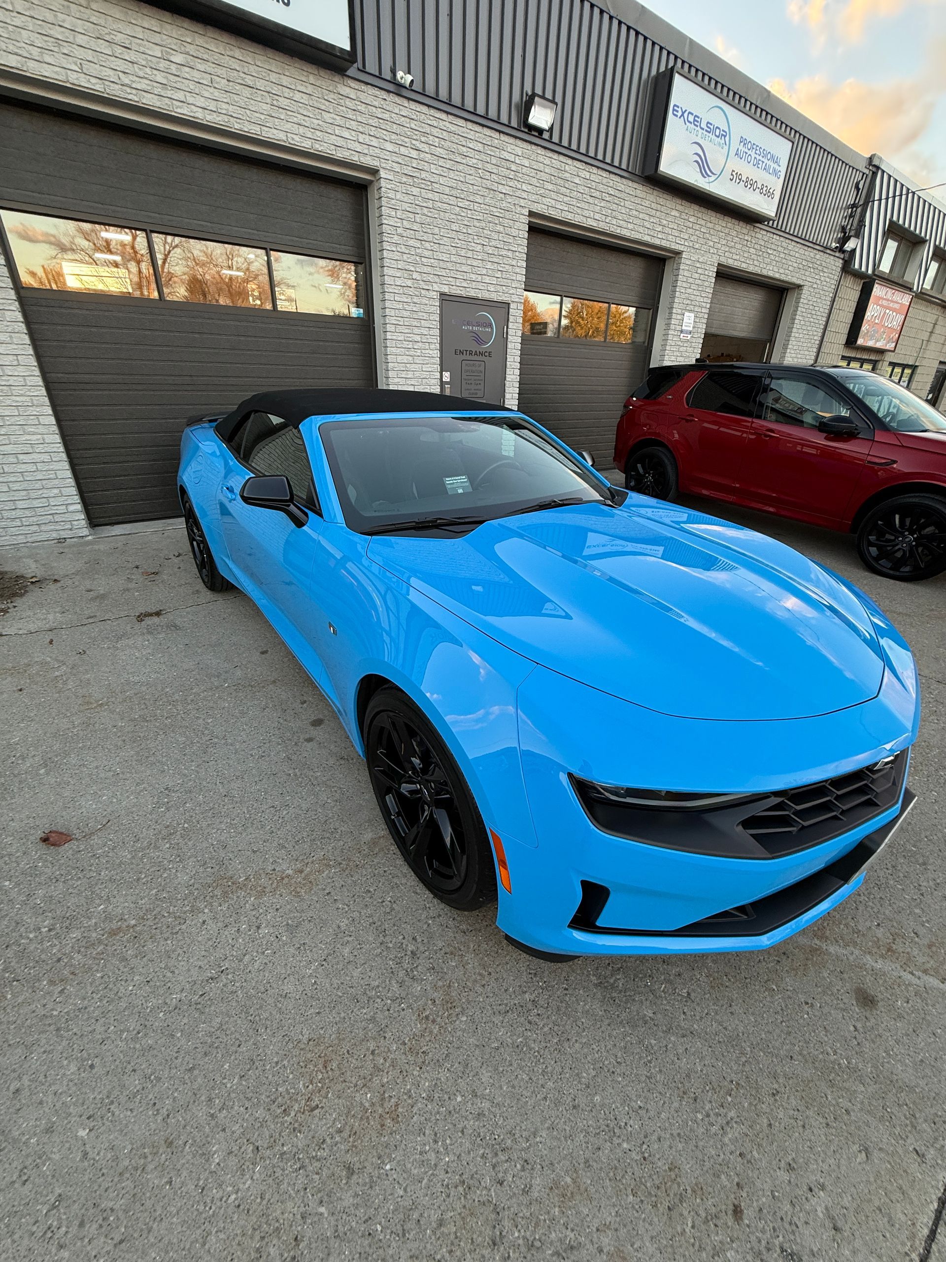 Bright blue convertible sports car parked outside a garage beside a red car