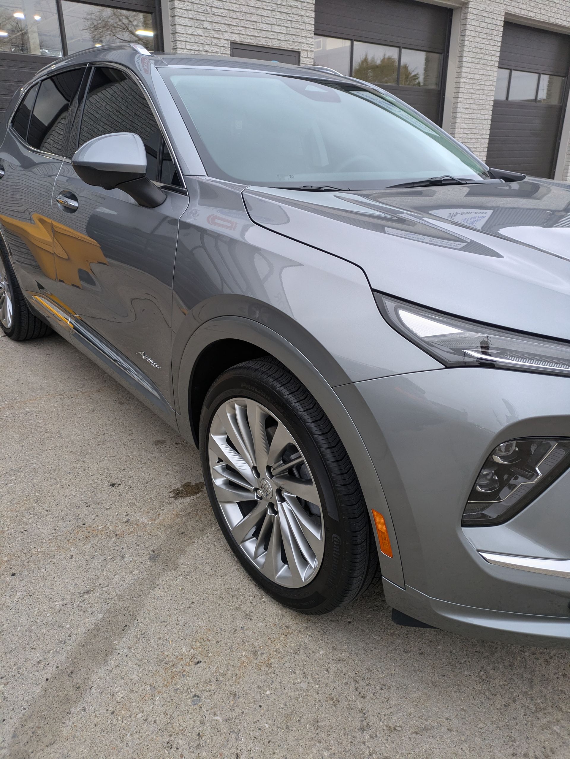 A gray car is parked on the side of the road in front of a building.