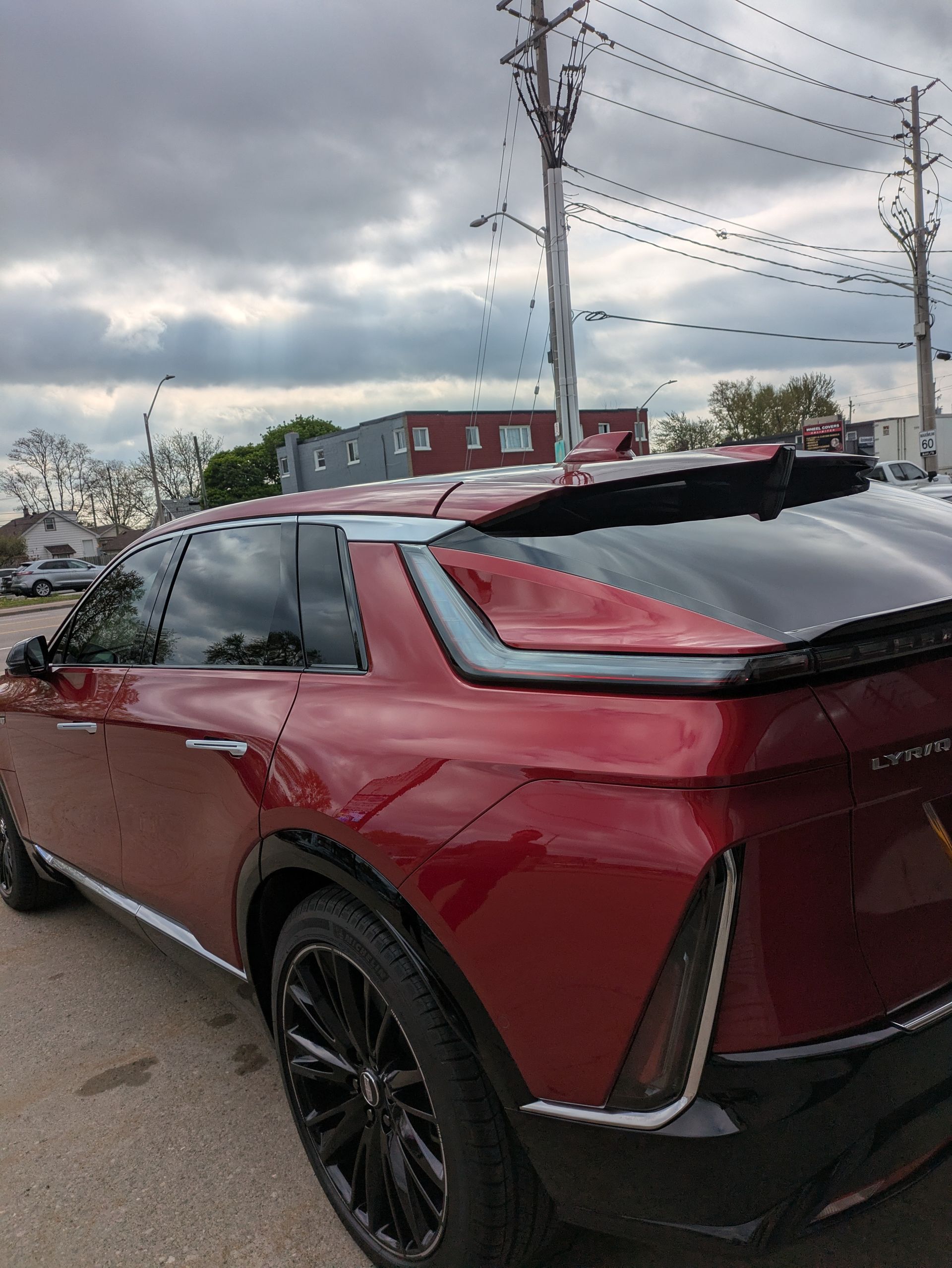 Red Cadillac Lyriq parked on a street, with dark tinted windows and black wheels. Cloudy sky.