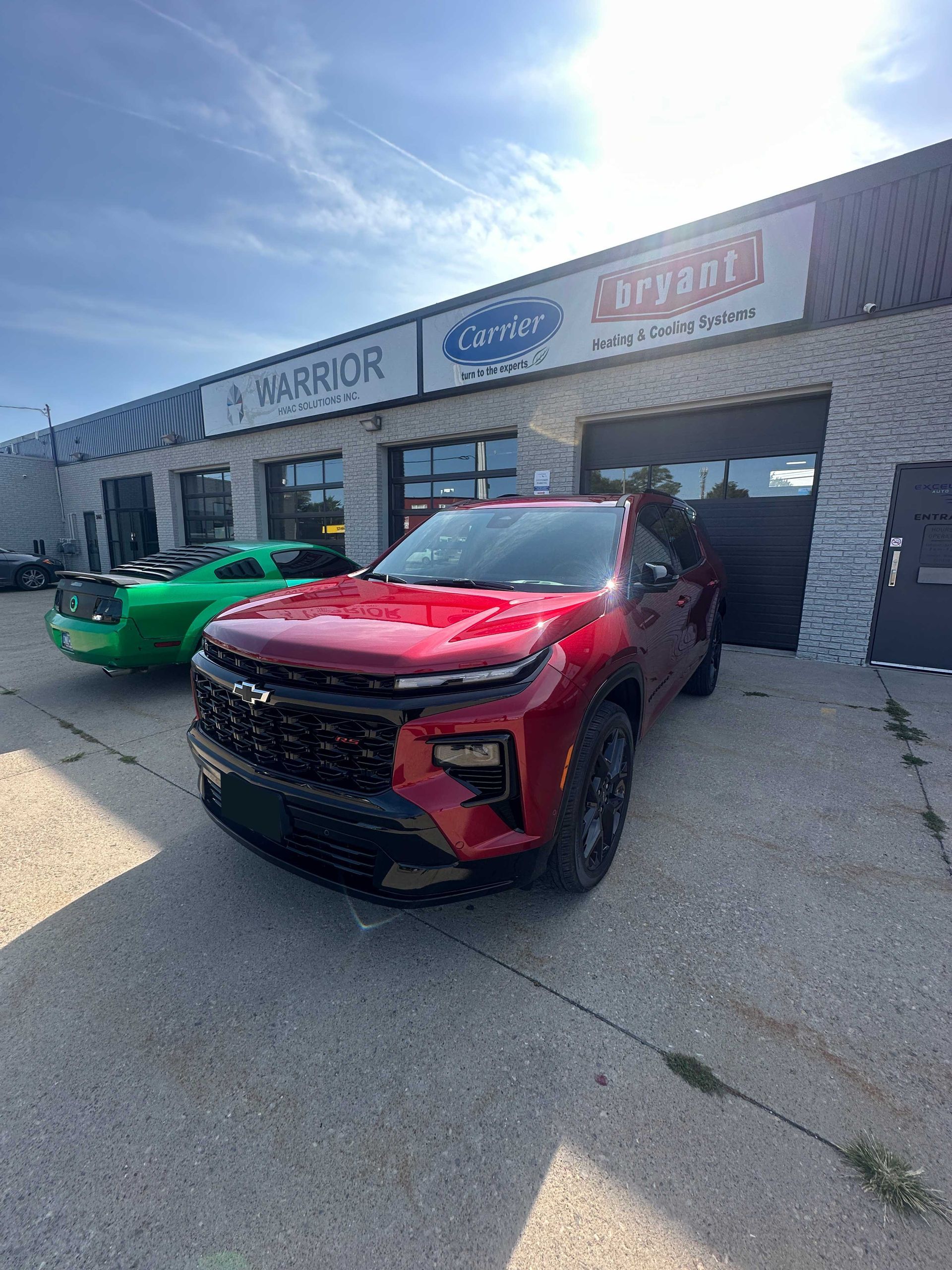 Red SUV parked outside an auto dealership, with a green car beside it on a sunny day.