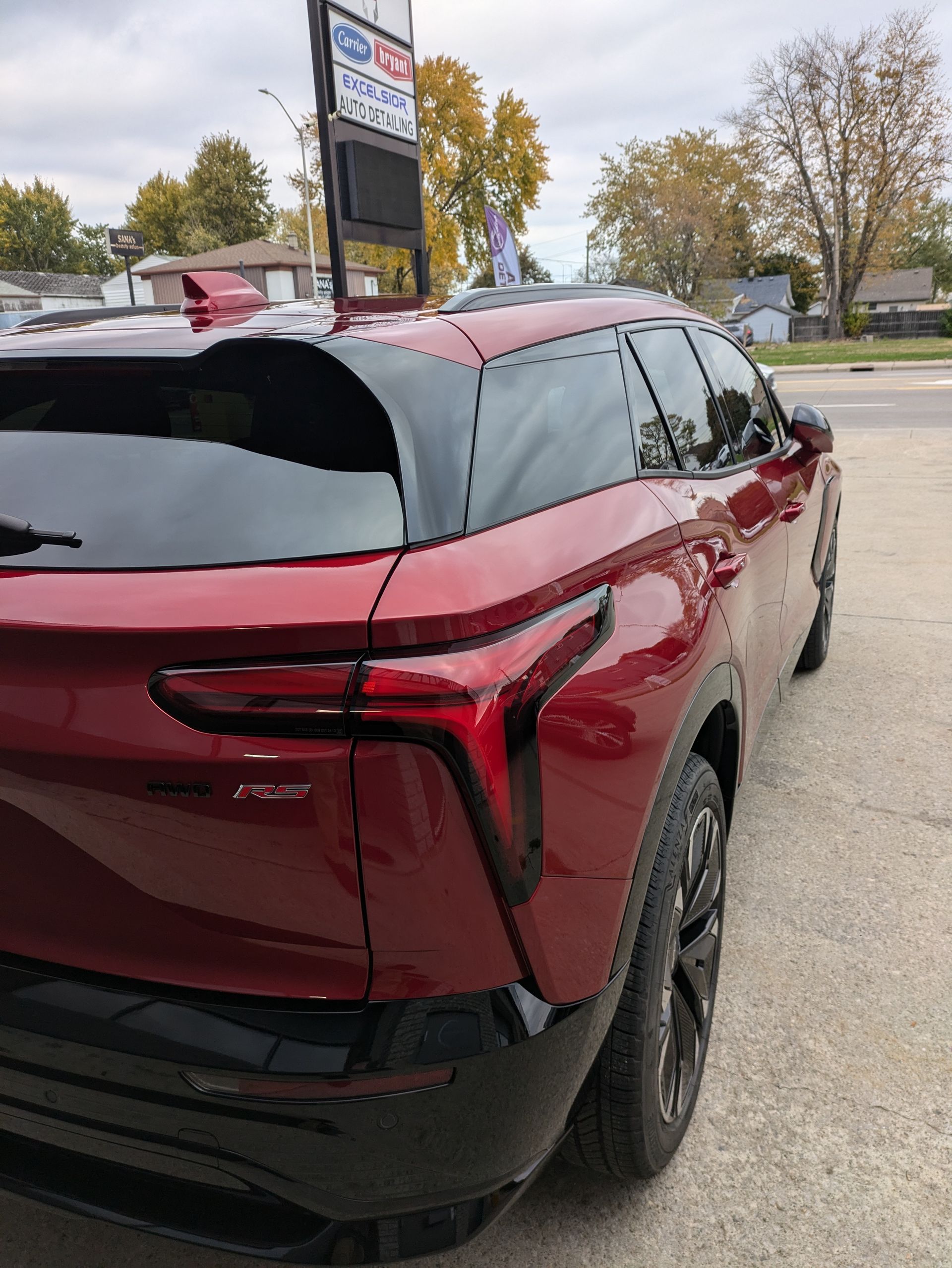 A red car is parked on the side of the road in front of a gas station.
