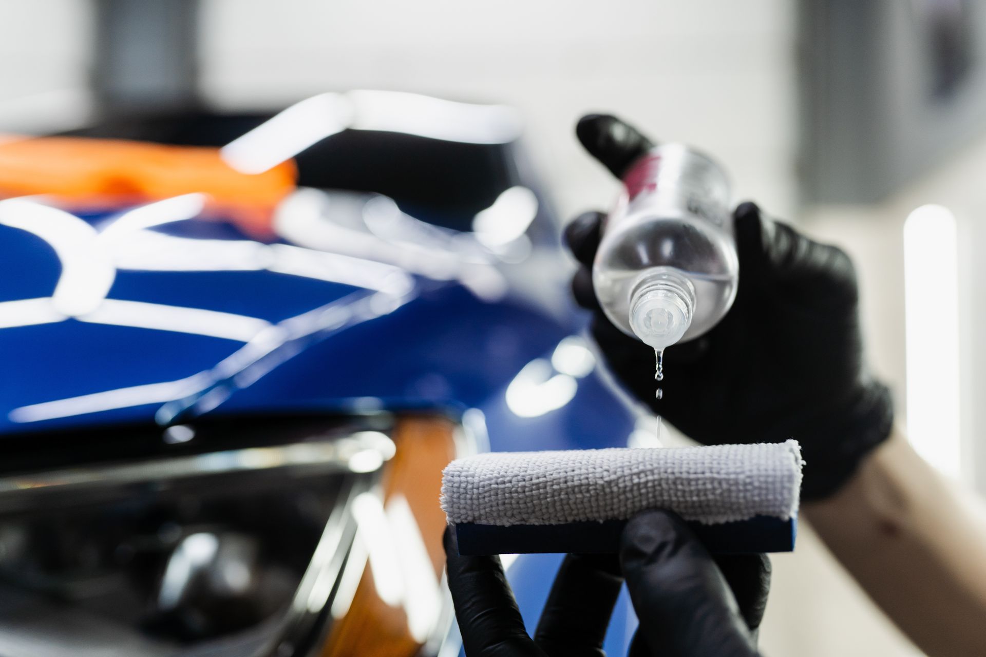 Gloved hand spraying liquid onto a blue car surface during detailing