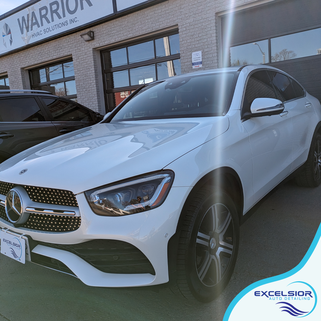 A white car is parked in front of a car dealership.