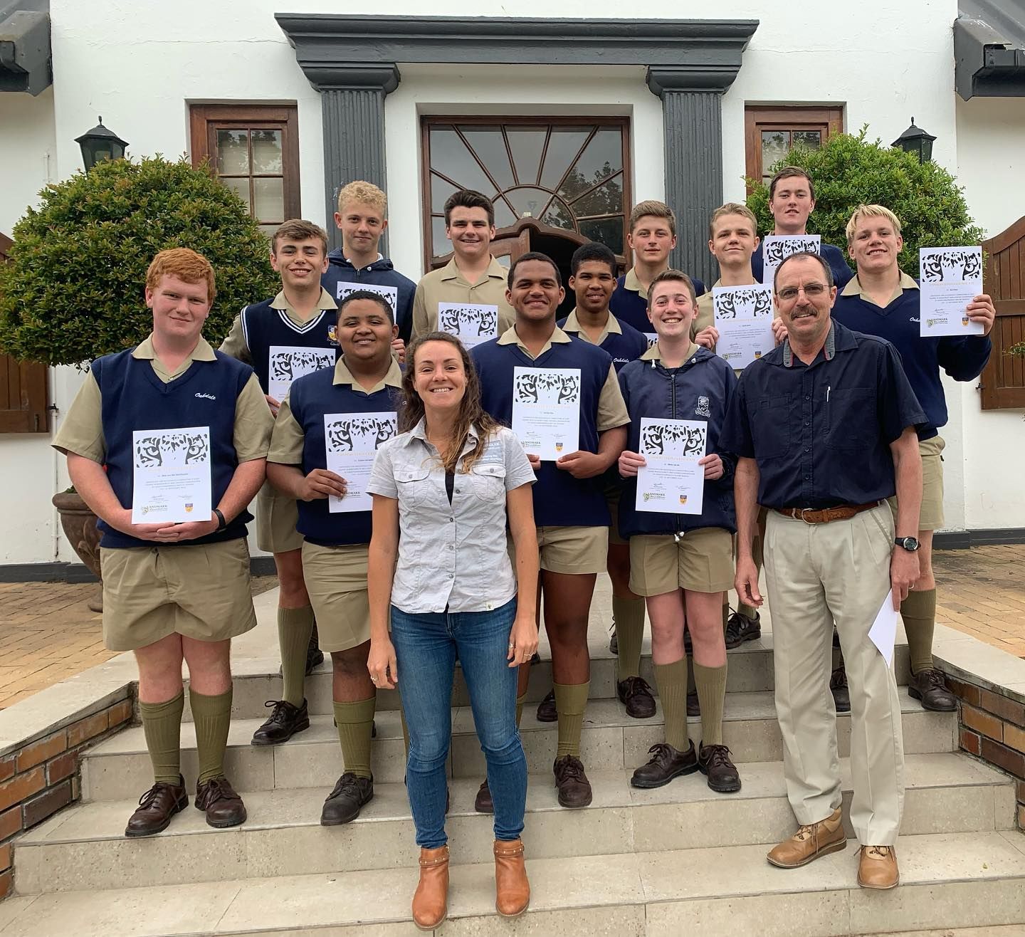 Group of students and adults holding certificates in front of a building.