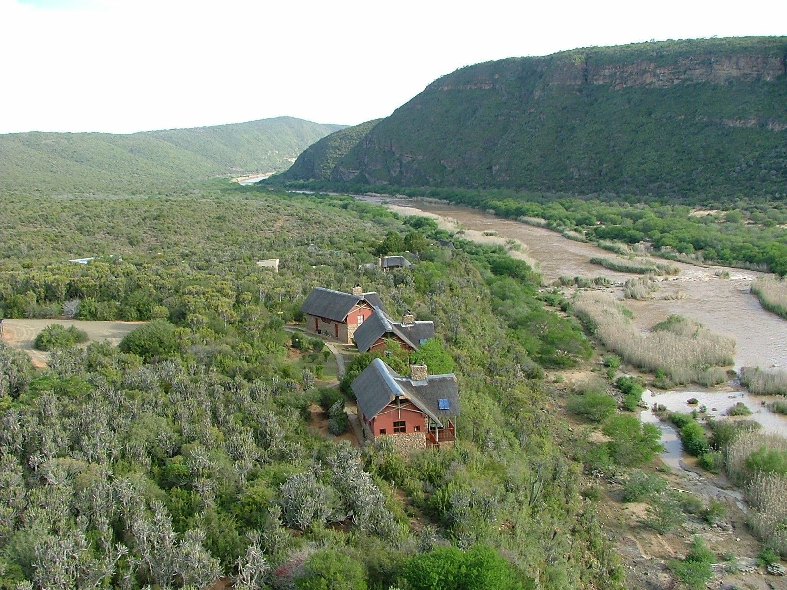 Cottages on a hillside next to a river, surrounded by green landscape and a mountain backdrop.