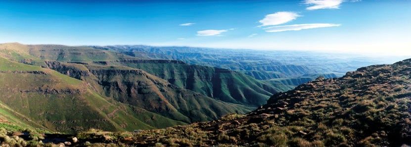 Panoramic view of a green, rugged mountain landscape under a clear blue sky.