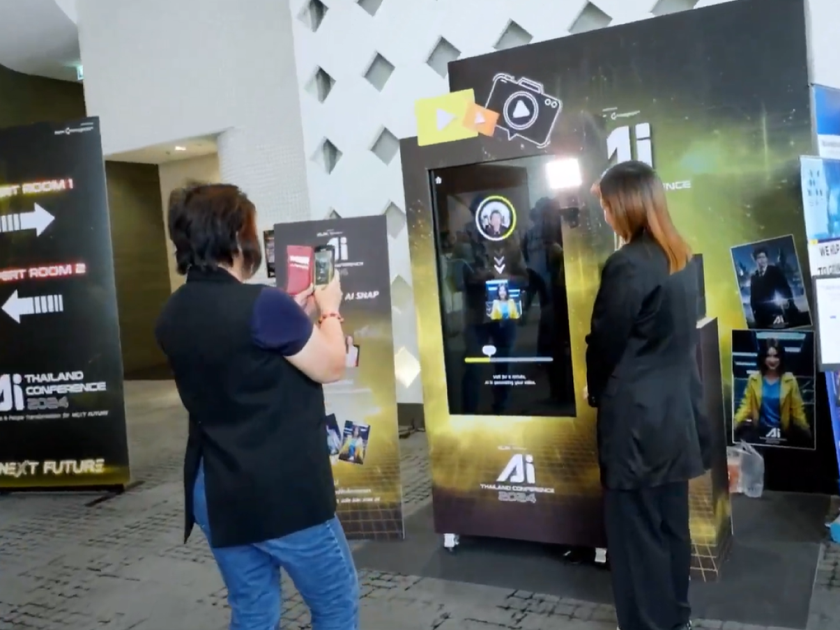 Two people at a glowing kiosk display in a lobby, one taking a photo with a phone.