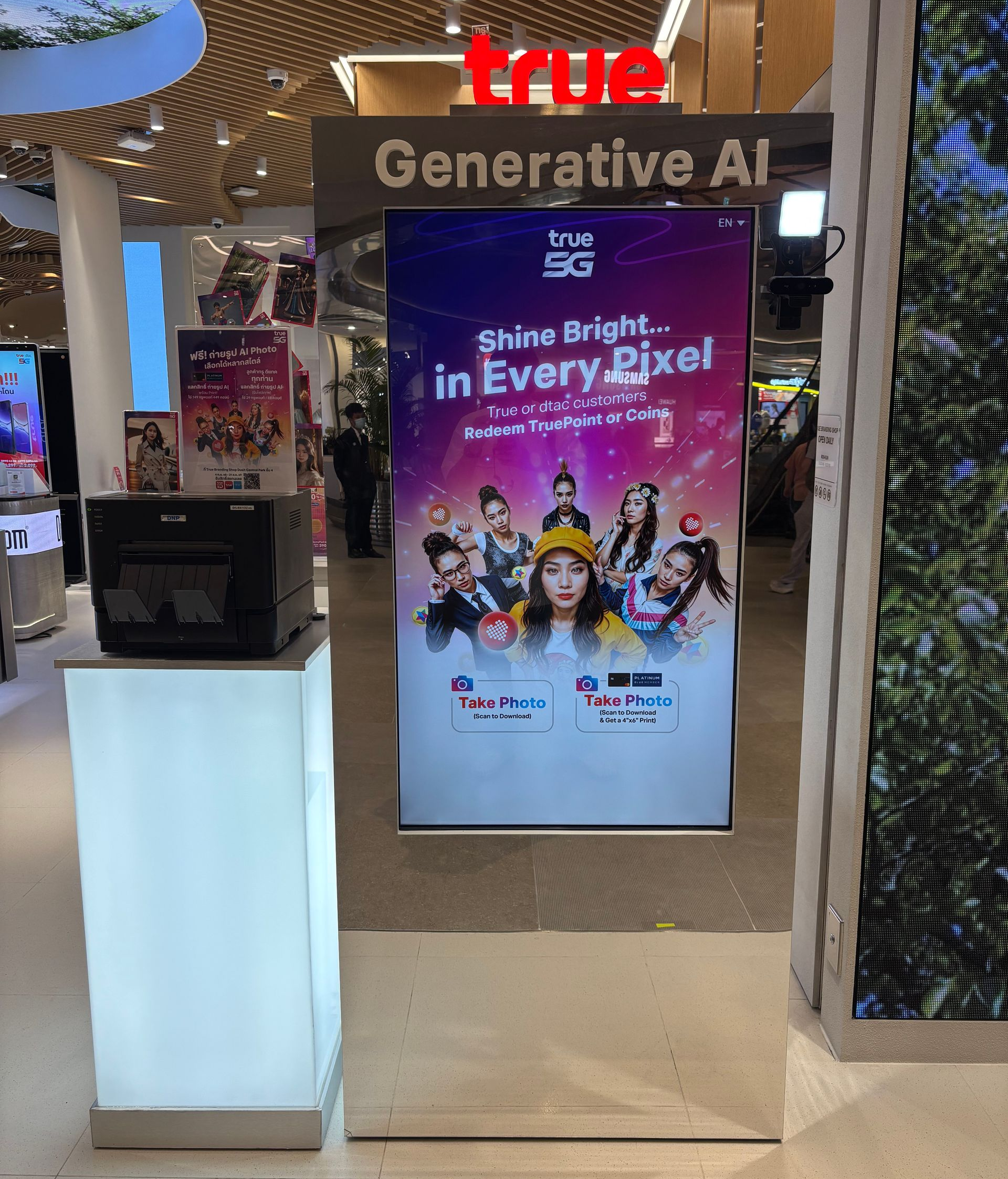 True Generative AI kiosk with colorful “Shine Bright in Every Pixel” poster in a mall display area