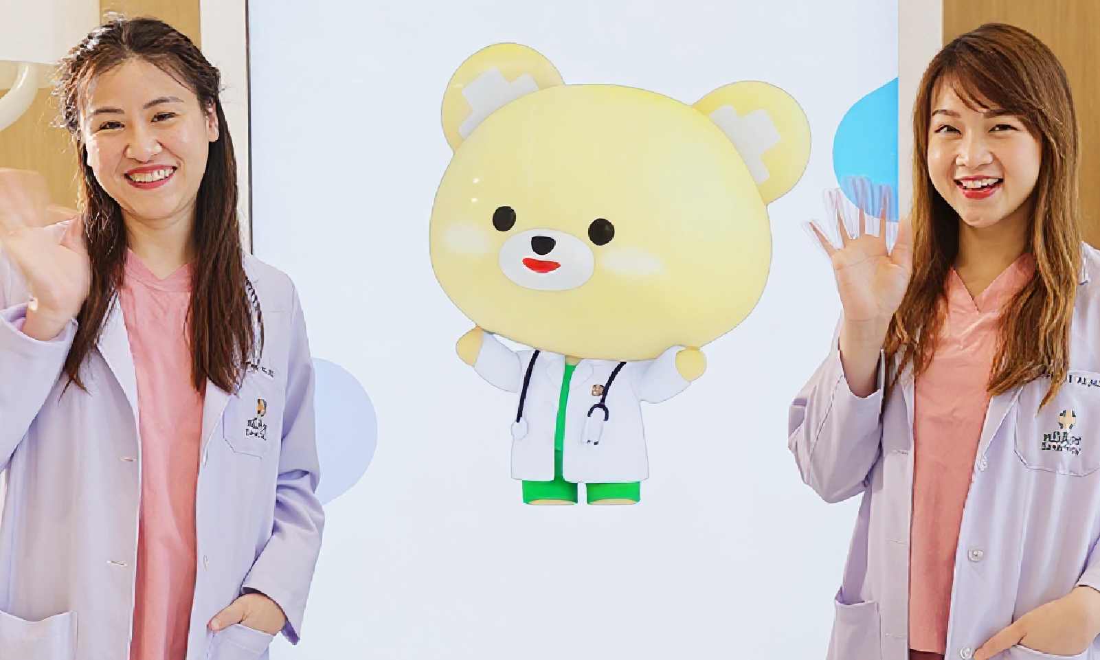 Two smiling women beside a yellow cartoon bear mascot in white coats on a pastel background