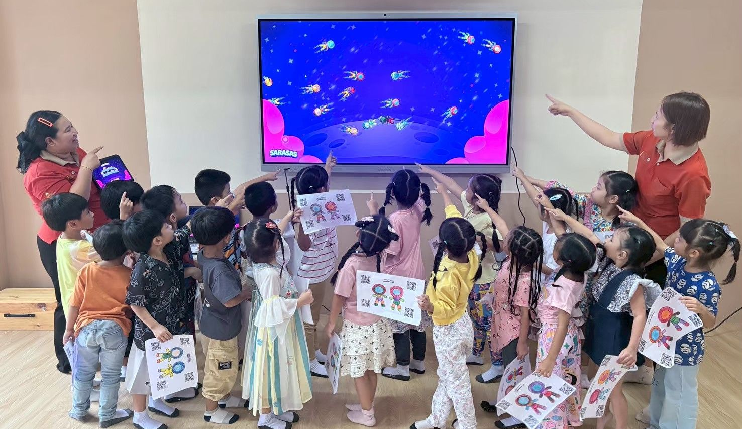 Children gathered in a classroom, watching and pointing at a colorful screen with fish underwater.