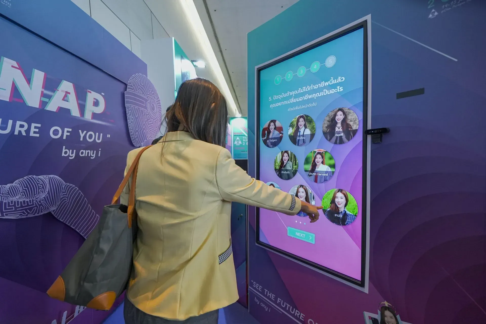 Person interacting with a touchscreen display at a purple event booth with photo thumbnails.