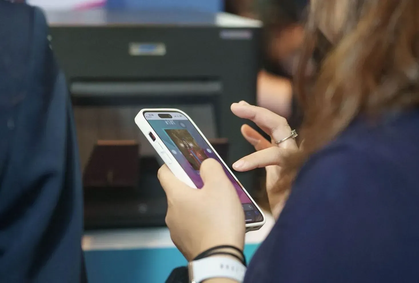 Person using a smartphone at a desk, with another hand gesturing nearby.