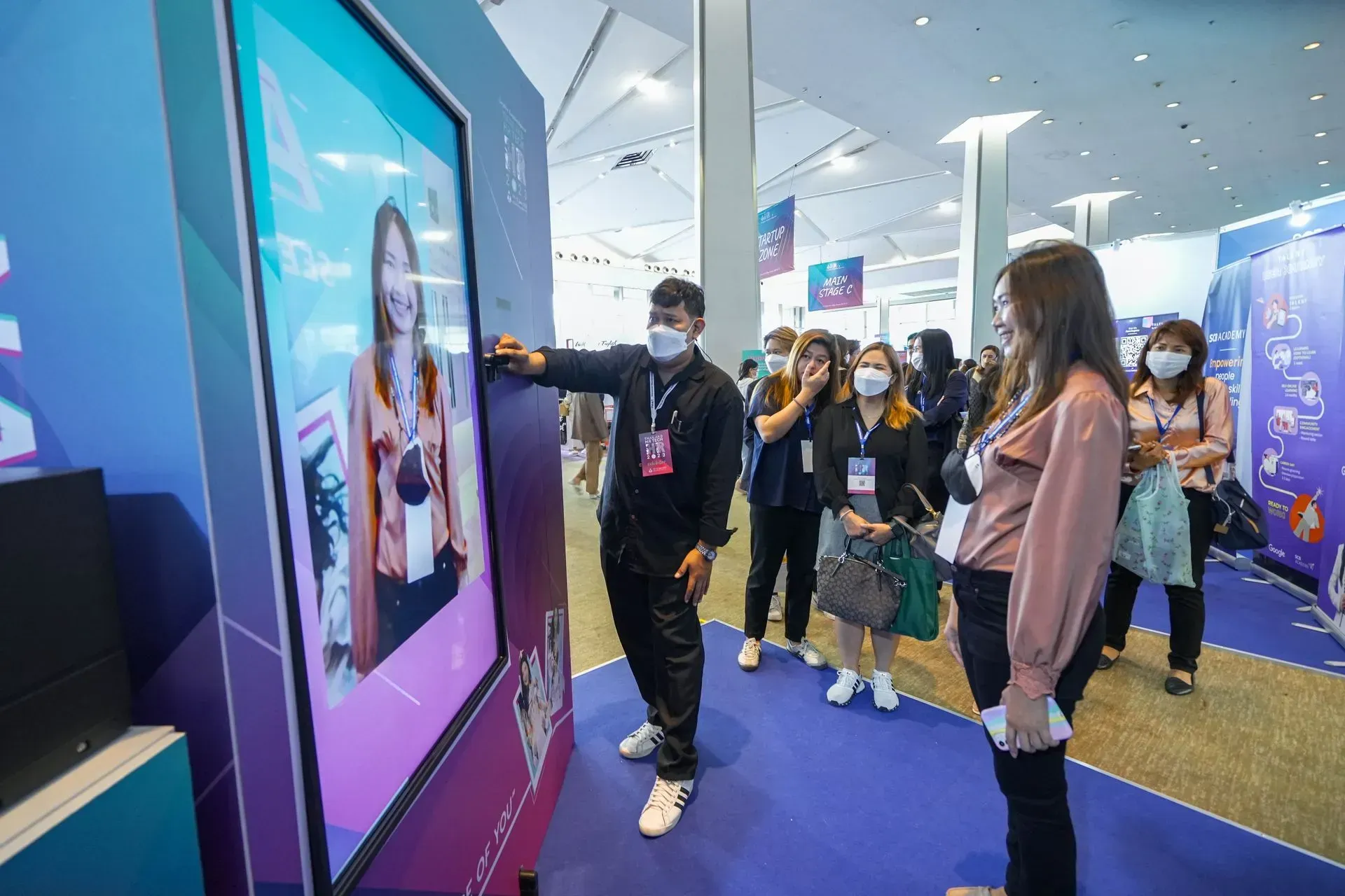 People at an indoor expo interacting with a large touchscreen display.