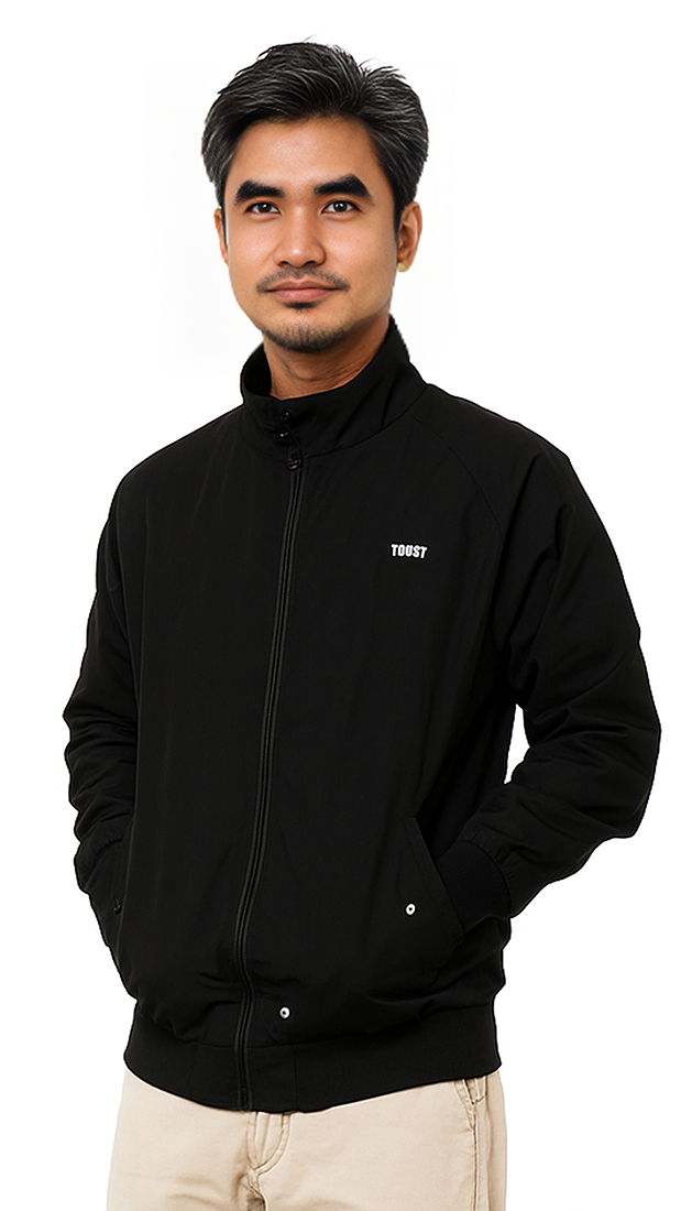 Man in a black jacket standing against a white background with hands in pockets.