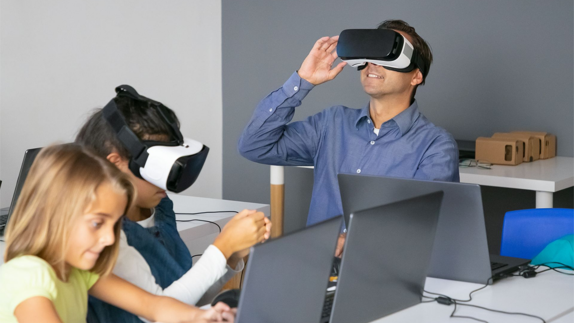People using VR headsets at a desk with laptops in a modern office