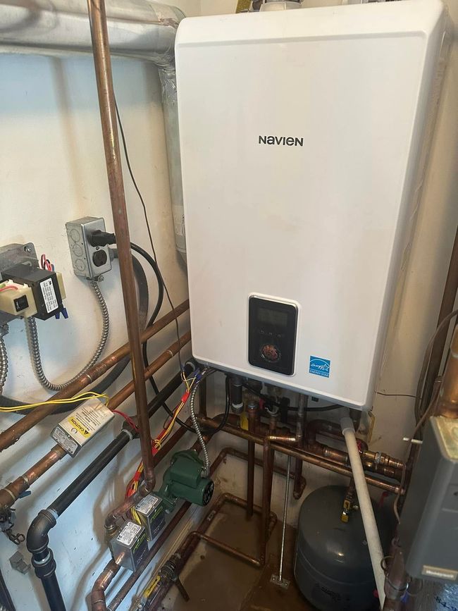 Boiler room with a white wall-mounted heating unit, copper pipes, and utility equipment.
