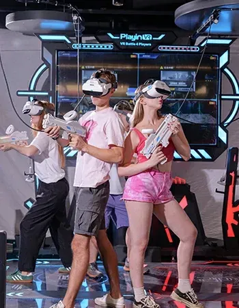 Three people in a neon-lit VR gaming center wear headsets and hold plastic toy guns while playing a virtual game.