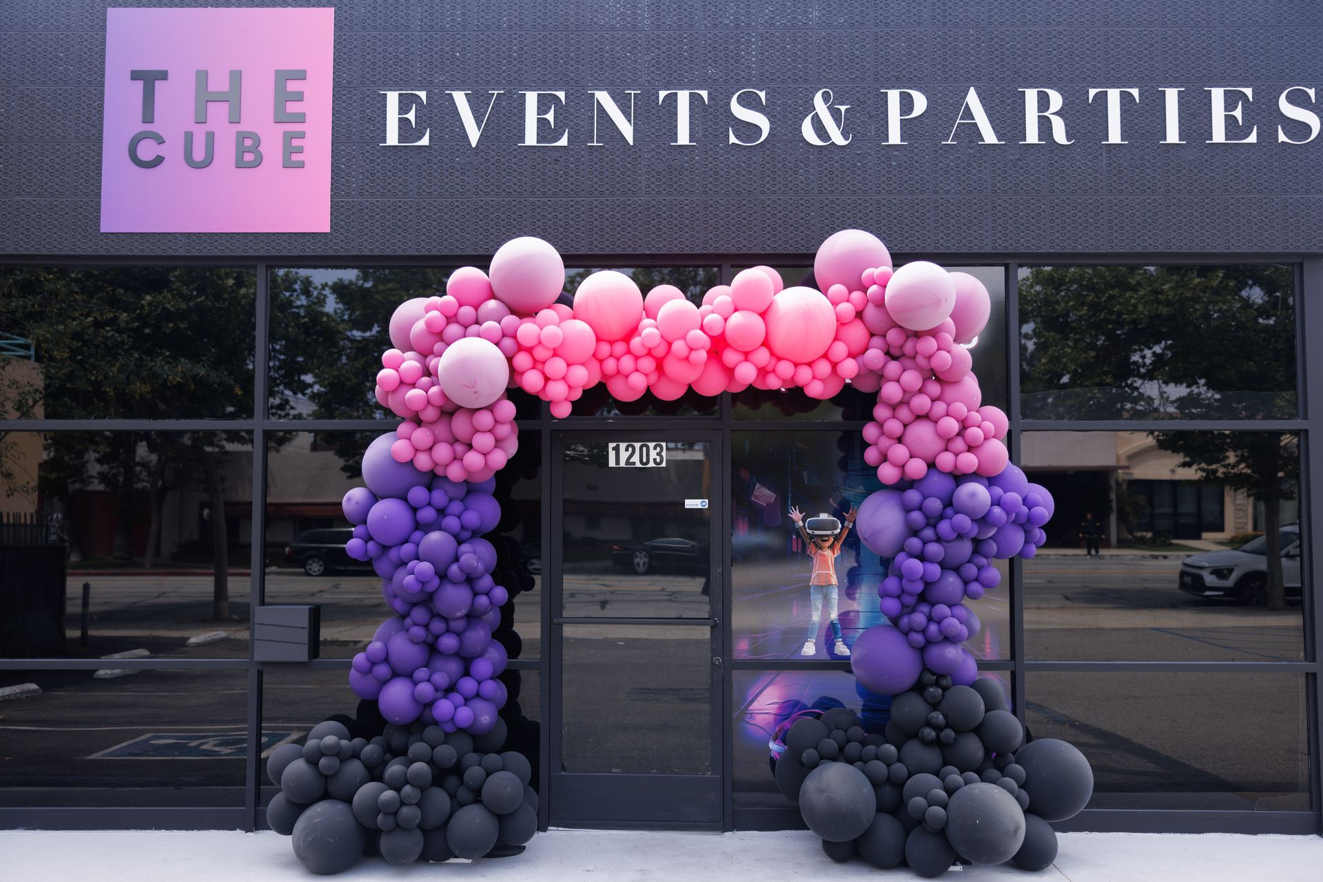 An entrance decorated with an arch of black, purple, and pink balloons in front of