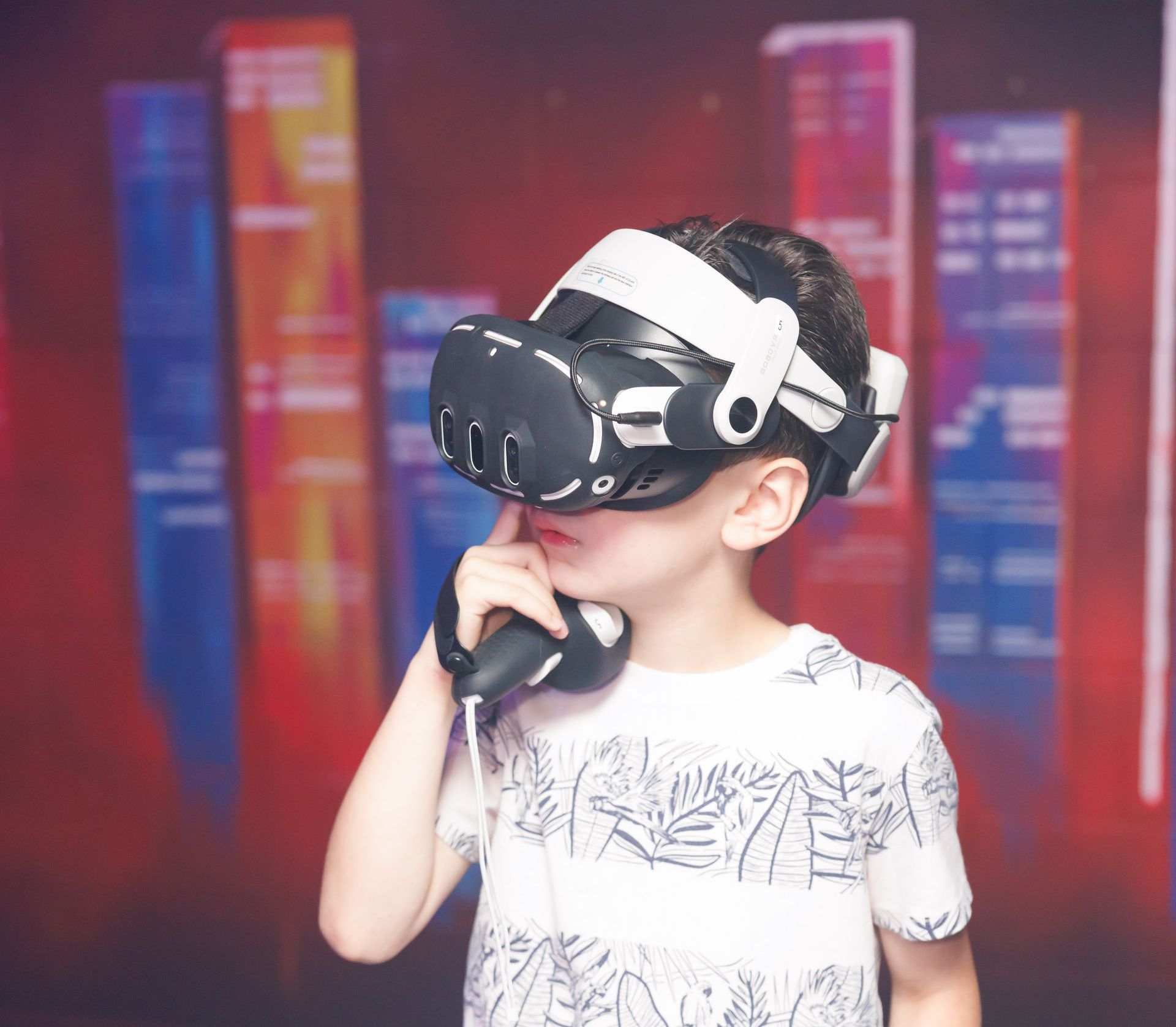 A person wearing a VR headset and holding a controller against their chin in front of a red abstract city-scape backdrop.