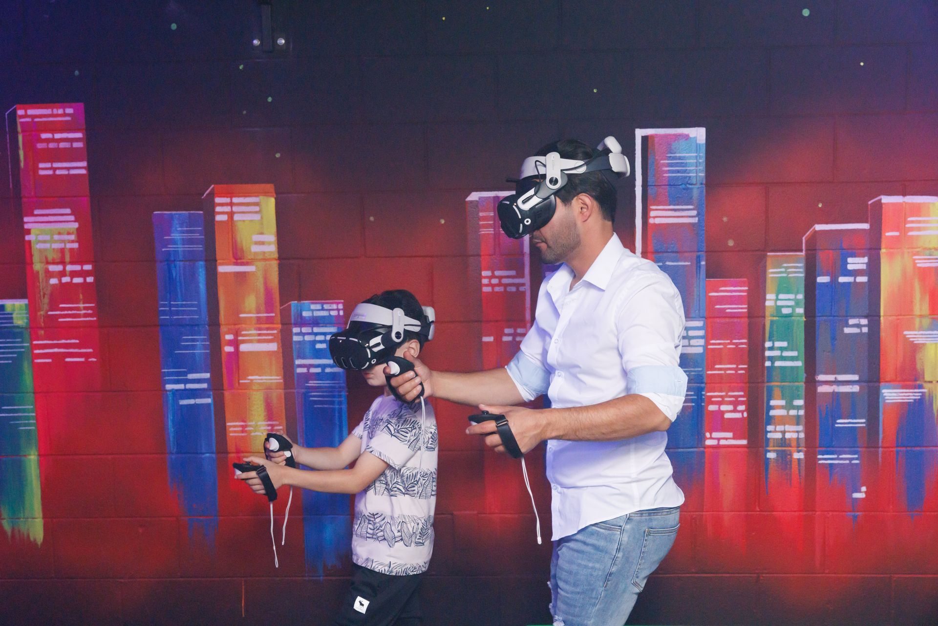 An adult and a child wear VR headsets and hold controllers while standing in front of a colorful, abstract city backdrop.