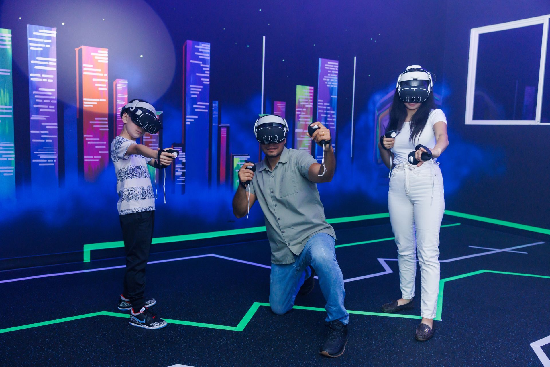 Three people wearing VR headsets and holding controllers pose in a neon-lit, futuristic room with glowing city graphics.