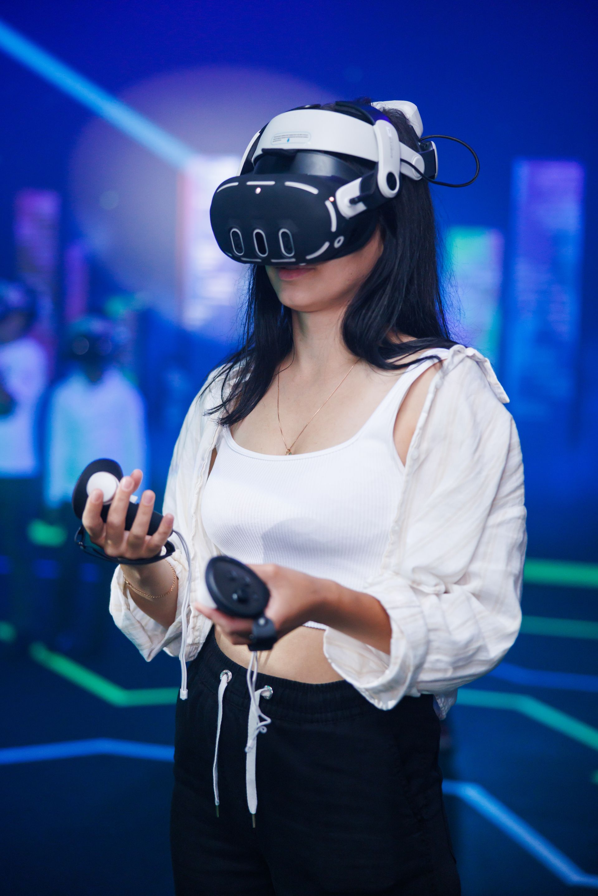 A person wearing a VR headset and holding controllers stands in a dimly lit, blue-toned space with digital floor lines.