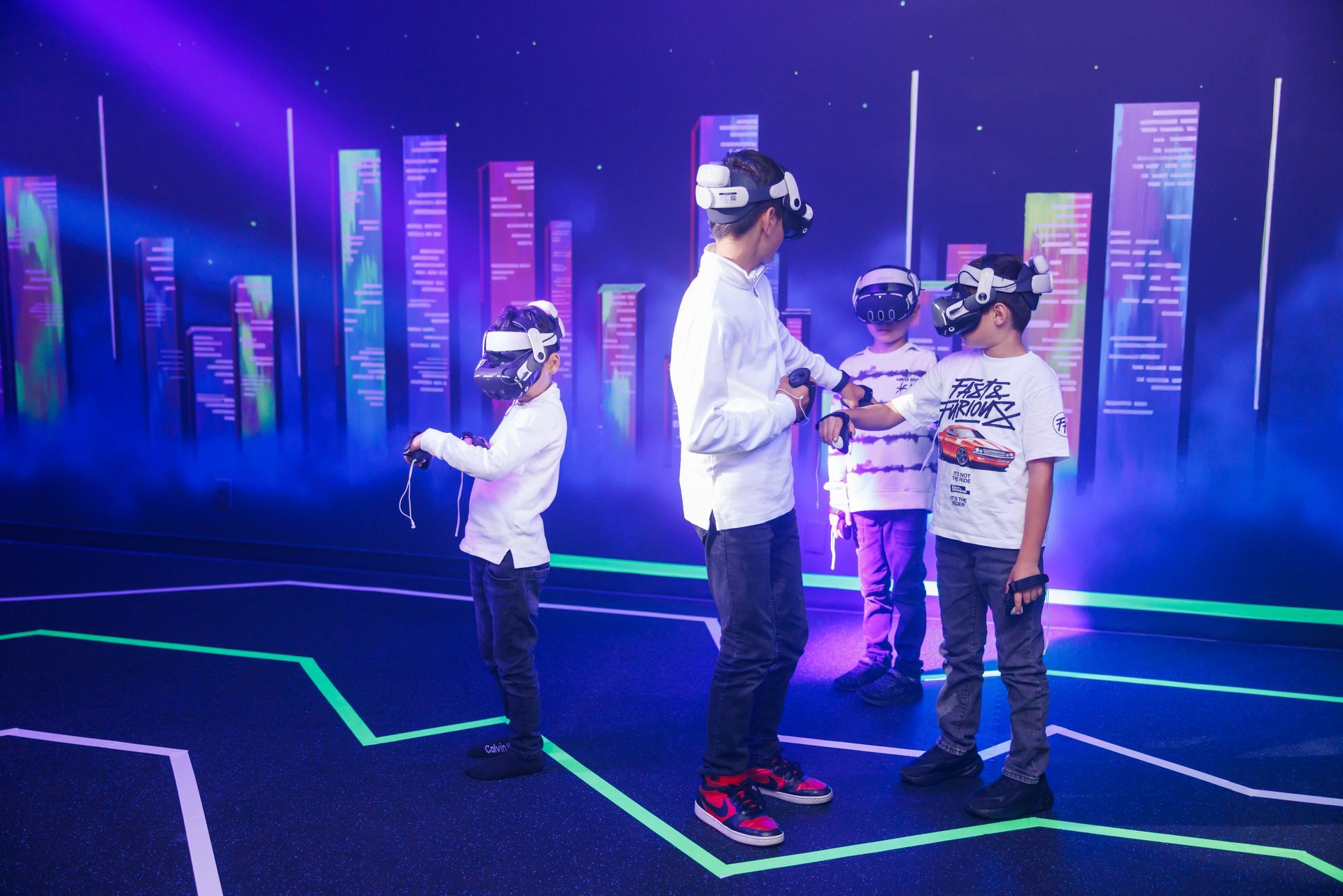 Four people wearing VR headsets stand on a stage with neon floor markings and purple-lit pillars in the background.